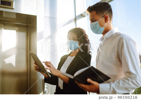 Two coworkers in protective face masks discussing project. Work in office during quarantine. Covid Two coworkers in protective face masks discussing project. Work in office during quarantine. Covid 96500216