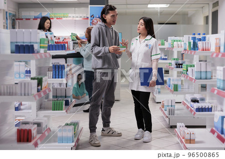 Asian man and specialist talking about vitamins box and explaining supplements leaflet in pharmacy store. Pharmacist giving package of medicaments and medical supplies, drugstore assistance. Asian man and specialist talking about vitamins box and explaining supplements leaflet in pharmacy store. Pharmacist giving package of medicaments and medical supplies, drugstore assistance. 96500865