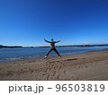 晴れた日の砂浜で、両手足を広げてジャンプする男性 96503819