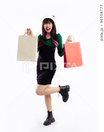 Asian girl in green and black dress wear santa hat carrying paper shopping bag posing full length white background. Asian girl in green and black dress wear santa hat carrying paper shopping bag posing full length white background. 96508777