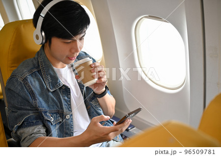 Asian male passenger listening to music through his headphones during flight Asian male passenger listening to music through his headphones during flight 96509781