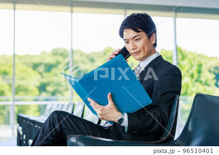 ロビーで資料を見ながら電話をするビジネスマン ロビーで資料を見ながら電話をするビジネスマン 96510401