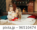 Cheerful mom and daughter play with Christmas lights on the floor by the fireplace, decorate the room for the holidays. The concept of Christmas and New Year 96510474