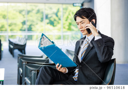 ロビーで資料を見ながら電話をするビジネスマン ロビーで資料を見ながら電話をするビジネスマン 96510618