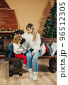 Cute mom and daughter are looking through a family photo album on Christmas Eve, spending time together by the fireplace and the Christmas tree. Christmas, New Year, memories, family evening 96512305