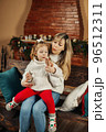 Happy mom and baby daughter reading having fun by the fireplace on Christmas or New Year's Eve. Parenthood, childhood, time together, holidays 96512311