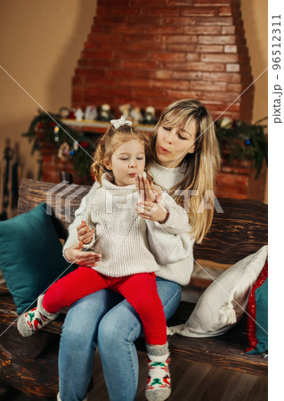 Happy mom and baby daughter reading having fun by the fireplace on Christmas or New Year's Eve. Parenthood, childhood, time together, holidays 96512311