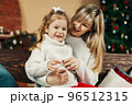 Mom and daughter in casual clothes play and hug against the background of a Christmas tree. Christmas and New Year, Christmas holidays, Christmas time. Childhood, motherhood, time together 96512315