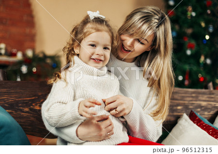 Mom and daughter in casual clothes play and hug against the background of a Christmas tree. Christmas and New Year, Christmas holidays, Christmas time. Childhood, motherhood, time together 96512315