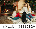 Happy mom and daughter play with their dachshund dog on the floor by the fireplace and Christmas tree 96512320