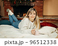 A charming young woman lies on a rug by the fireplace on Christmas Eve 96512338