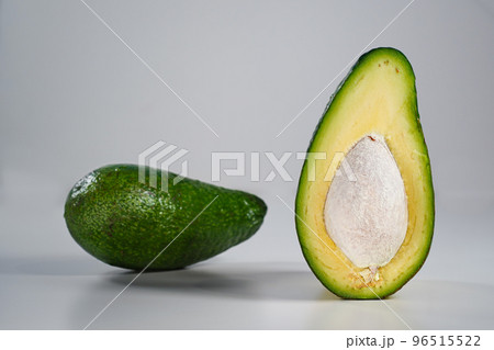 Avocado in section with seed close-up at eye level, space for text, light gray background. Half of an avocado, white porous coating of the seed, stands upright, a whole fruit in green peel blurred 96515522