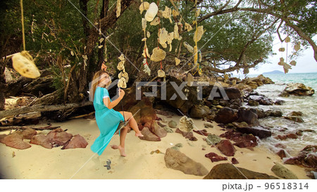 Pretty woman swinging on a swing on a tropical beach, on shores of the turquoise sea. Concept travel, walks, rest in sea, tropical resort coastline relaxation traveling tourism summer holidays. Pretty woman swinging on a swing on a tropical beach, on shores of the turquoise sea. Concept travel, walks, rest in sea, tropical resort coastline relaxation traveling tourism summer holidays. 96518314
