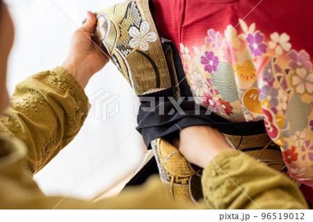 若い女性に振袖の着付けしているところ 96519012