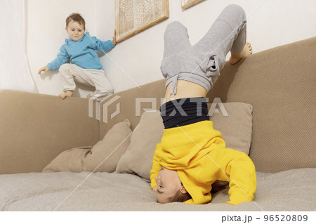 Two active, little kids doing gymnastic handstand exercise in living room. Child standing on hands upside down. Brothers relationship. Children spending time together, having fun during sport. Two active, little kids doing gymnastic handstand exercise in living room. Child standing on hands upside down. Brothers relationship. Children spending time together, having fun during sport. 96520809