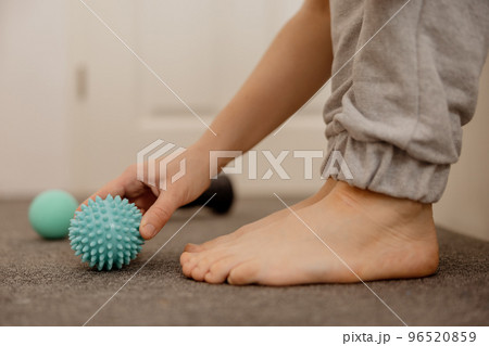 Woman doing flatfoot correction gymnastic exercise using massage ball. Myofascial relaxation of foot muscles. Hallux valgus. Pain. Identification of flat feet. Self care practices at home, healthcare. Woman doing flatfoot correction gymnastic exercise using massage ball. Myofascial relaxation of foot muscles. Hallux valgus. Pain. Identification of flat feet. Self care practices at home, healthcare. 96520859