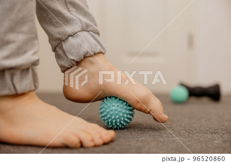 Woman doing flatfoot correction gymnastic exercise using massage ball. Myofascial relaxation of foot muscles. Hallux valgus. Pain. Identification of flat feet. Self care practices at home, healthcare. Woman doing flatfoot correction gymnastic exercise using massage ball. Myofascial relaxation of foot muscles. Hallux valgus. Pain. Identification of flat feet. Self care practices at home, healthcare. 96520860