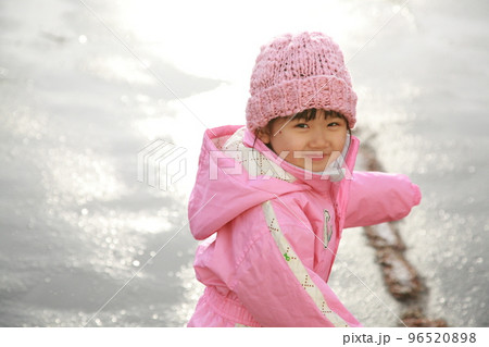 雪解け水に濡れたアスファルトに太陽の光が反射する中で走り回る3歳の女の子 96520898