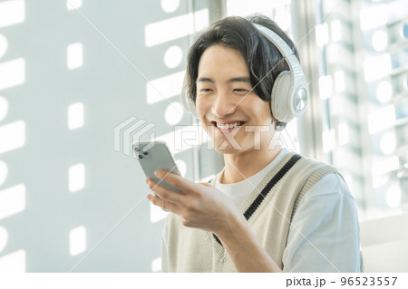 木漏れ日の中ヘッドフォンをしてスマホで音楽を聴く若者 96523557