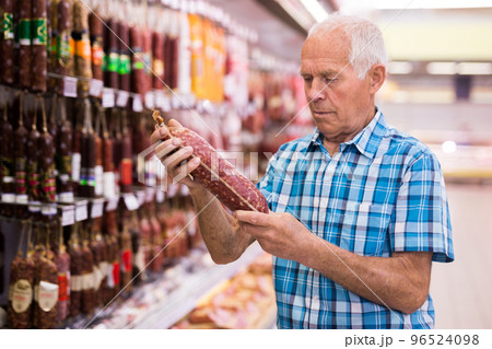 mature senor choosing uncooked smoked sausages in sausage department supermarket 96524098