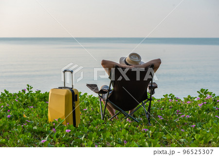 Man sitting on the chair beside suitcase at the beach, vacation, relaxing time concept. 96525307