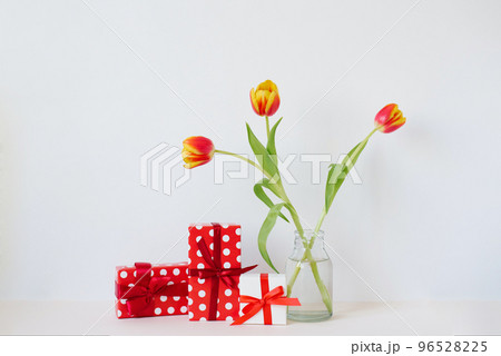 A vase with a bouquet of beautiful tulips and gift boxes on the table. Greeting card for Valentine's Day, March 8, Mother's Day A vase with a bouquet of beautiful tulips and gift boxes on the table. Greeting card for Valentine's Day, March 8, Mother's Day 96528225