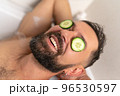 man with cucumber on front of his eyes relaxing in bath at home 96530597