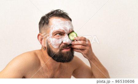 Funny man with cucumber and beauty mask on face in bath at home 96530606