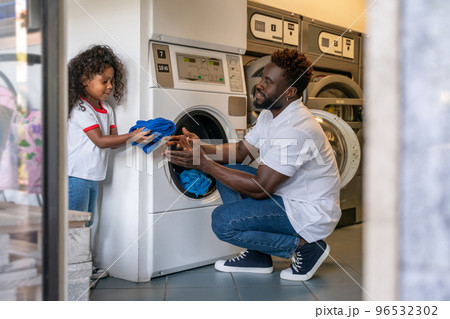 Man and his daughter putting laundry into a washer 96532302