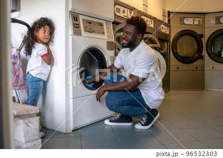 Father loading dirty clothes into a washer in daughter presence 96532303