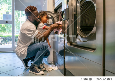 Father and daughter loading laundry into a washer 96532304