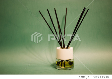 Fragrance diffuser perfume freshener with black sticks on green emerald background with space for text. Decor accessories for modern interior. Home aroma isolated. Air refresher bottle. Apple scent. 96533540