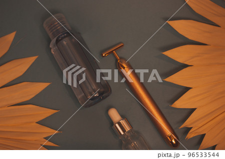 Vibrating golden facial massager, glass jar with oil dropper for massage on blue Vibrating golden facial massager, glass jar with oil dropper for massage on blue 96533544