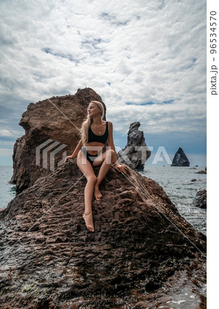 Woman swimsuit sea. Attractive blonde woman in a black swimsuit enjoying the sea air on the seashore around the rocks. Travel and vacation concept. Woman swimsuit sea. Attractive blonde woman in a black swimsuit enjoying the sea air on the seashore around the rocks. Travel and vacation concept. 96534570
