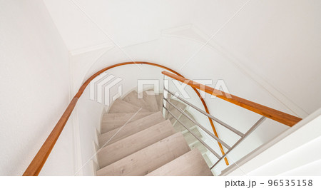 Spiral stairway with white stairs and wooden railing on wall inside of a house. Spiral stairway with white stairs and wooden railing on wall inside of a house. 96535158