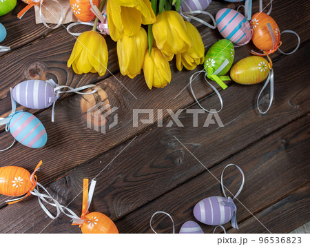 Several spring yellow tulips lie on a wooden board next to Easter eggs 96536823