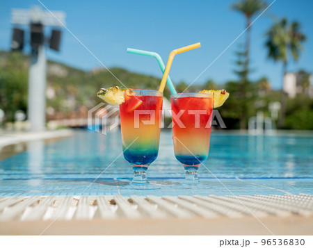 glasses with summer bright cocktails and drinking straws stand by the pool 96536830