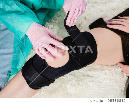 close-up of a family doctor putting a black brace on a patient's knee 96536852