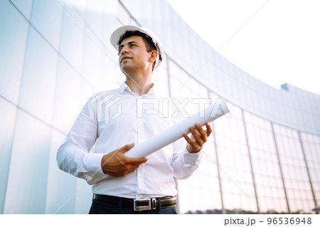 Young worker in a helmet and with a phone at a work object. Business, building 96536948