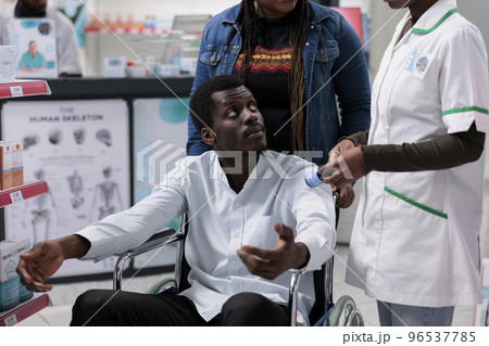 Pharmacy consultant explaining man with disability medications instruction, customer in wheelchair choosing nutritional supplements. Pharmacist recommending medicaments to client Pharmacy consultant explaining man with disability medications instruction, customer in wheelchair choosing nutritional supplements. Pharmacist recommending medicaments to client 96537785