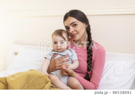 Love and tenderness, motherhood concept. Loving mother caressing her cute baby daughter, lying together on bed 96538091