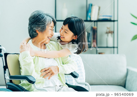 リビングで団らんする車椅子の祖母と小学生の孫娘 96540069