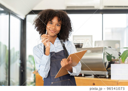 Portrait of a smiling young african american waitress wearing apron ready to take customer order 96541073