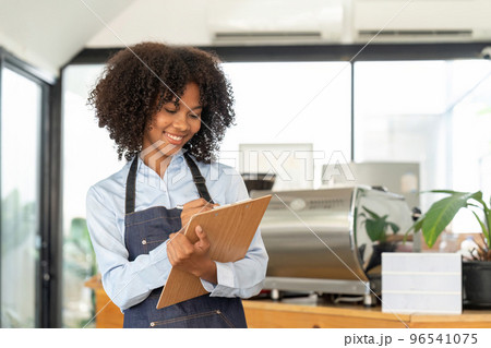 Portrait of a smiling young african american waitress wearing apron ready to take customer order 96541075