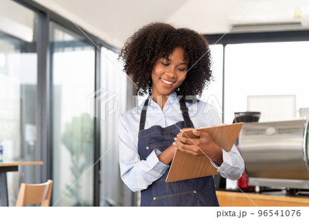 Portrait of a smiling young african american waitress wearing apron ready to take customer order 96541076