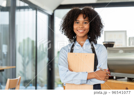 Portrait of a smiling young african american waitress wearing apron ready to take customer order Portrait of a smiling young african american waitress wearing apron ready to take customer order 96541077