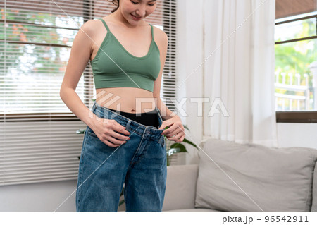 Sporty woman is smiling while wearing in loose big jean to showing successfully of weight loss Sporty woman is smiling while wearing in loose big jean to showing successfully of weight loss 96542911