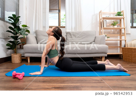 Young woman is practicing yoga with cobra pose during exercise on mat in her living room at home 96542953