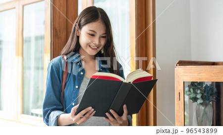 Young woman student is standing near the window and reading literature to relaxation while taking a break 96543899