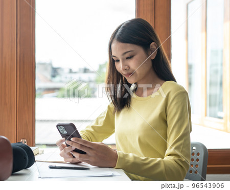 Young woman student in sweater is using smartphone to chatting with classmate while taking a break 96543906